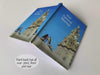 An open hardback notebook having a cover with an image of a pair of shoes on a wall with the cunard liverpool liver building in the background, with a personal message on the cover