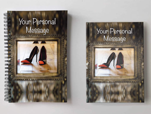 Two notebooks, side by side, both having covers with an image of a a mirror in a brass surrounding, a pair of orange and black high heels shoes are seen reflected in the mirror, with a personal message on the cover