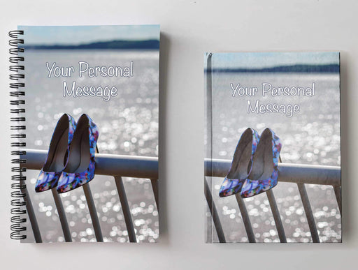 Two notebooks, side by side, both having covers with an image of a pair of shoes hung on a railing in front of an ocean, with a personal message on the cover