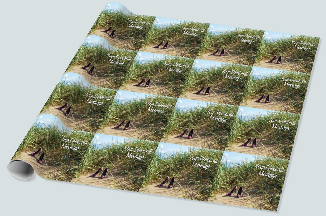 A roll of wrapping paper showing a pair of multicoloured high heel shoes on a beach in the sand hills, with sand hill grasses in close proximity to the shoes and a blue sky in the background, the image is repeated