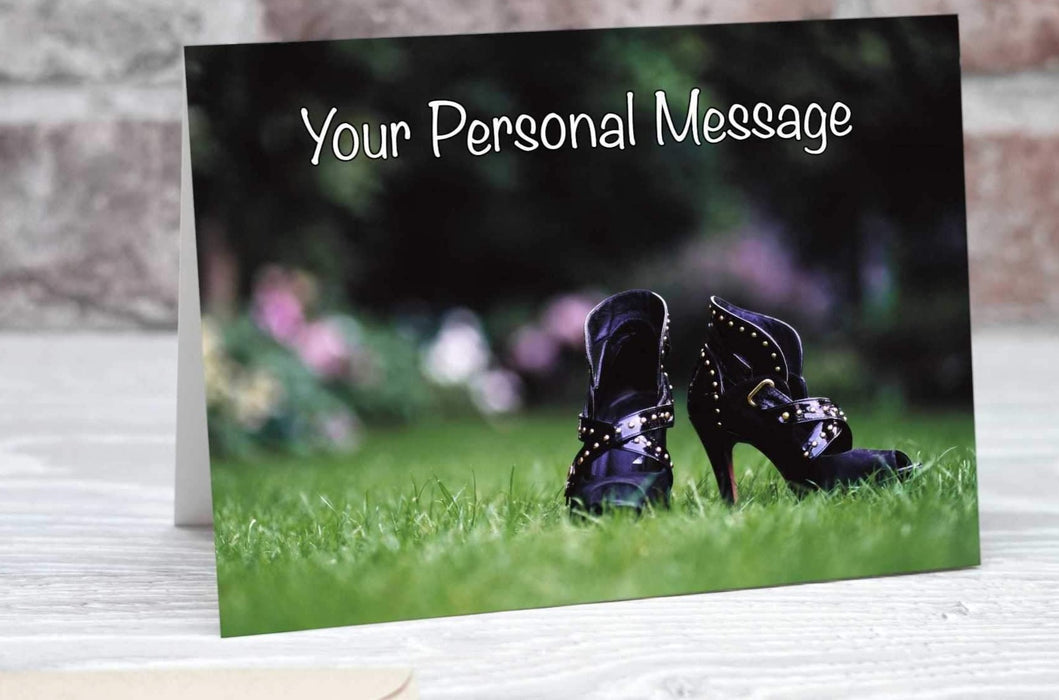 A greetings or birthday card showing a close up of pair of high heeled purple ankle boots on grass in a garden, with faint images of flowers in the background along with a perosnal message on the card