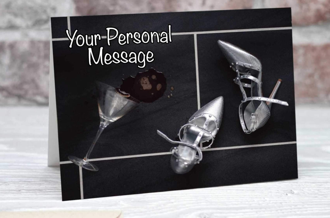 A birthday or greetings card showing a pair of silver high heel shoes on a black tiled floor, adjacent to the shoes is a cocktail glass on its side with a spilt drink on the floor, along with a personal message