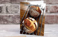 a birthday or greetings card on a desk with an envelope and pen, the card having an image of two sourdough loaves of bread adjacent to each other resting on a metal rack in an angled side on portrait viewpoint