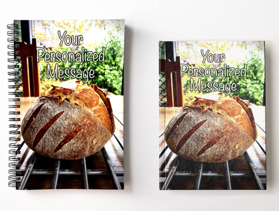 a pair of notebooks, one spiral bound, one hard back, next to each with image of a large sourdough loaf sat of a table with a garden in the back ground