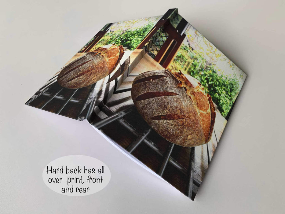 an open hard back notebook, with and image of a large sourdough loaf sat of a table with a garden in the back ground