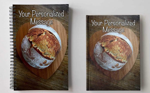 a pair of notebooks, one spiral bound, one hard back, next to each with image of a large sourdough loaf at on a heart shaped wooden tray