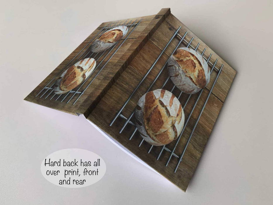 an open hard back notebook, with and image of two large sourdough loaves sat on a wire rack upon a table and seen from overhead