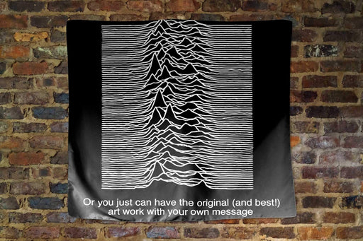 A black tapestry hung on a brick wall, the tapestry showing horizontal wavy lines in the style of a scope readout, the lines combine to form an image of the peace symbol
