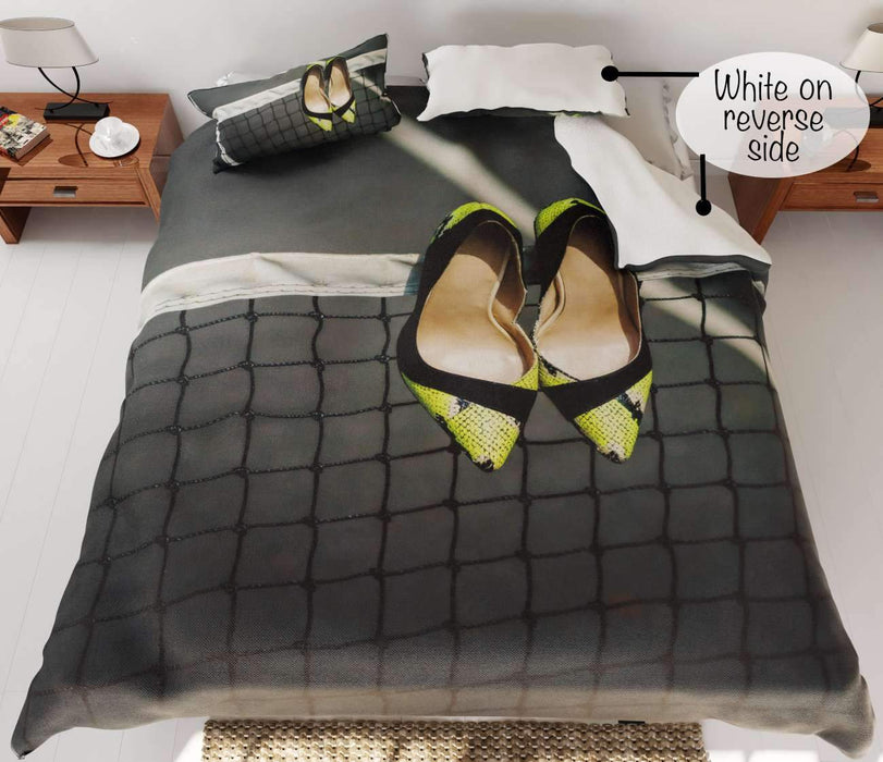 A duvet cover on a bed, the duvet cover having an image of a tennis court with a pair of yellow high heel shoes hung on the tennis net, the corner of the duvet is folded back to show white underside