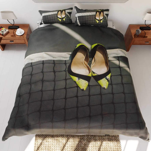 A duvet cover on a bed, the duvet cover having an image of a tennis court with a pair of yellow high heel shoes hung on the tennis net, along with a printed personal message on the duvet