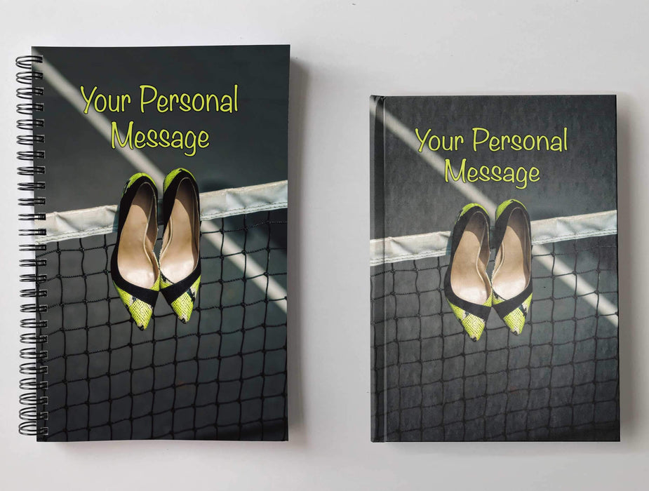 Two notebooks, side by side, both having covers with an image of a pair of yellow and black high heel shoes hanging from a tennis net and a personal message on the cover