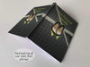 An open hardback notebook the cover having an image of a pair of yellow and black high heel shoes hanging from a tennis net and a personal message on the cover