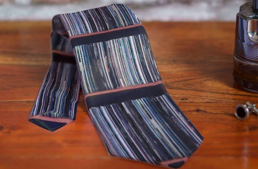 a rolled up tie on a bed side table, the tie having image of vinyl records on a shelf printed on it