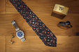 a neck tie laid flat showing a montage of record players on the tie, sited on a bed side table