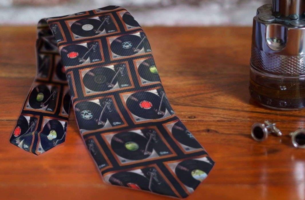 a partially rolled neck tie showing a montage of record players on the tie, sited on a bed side table