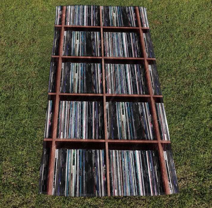 a towel with image of vinyl records stacked along shelves, the towel laid out on grass