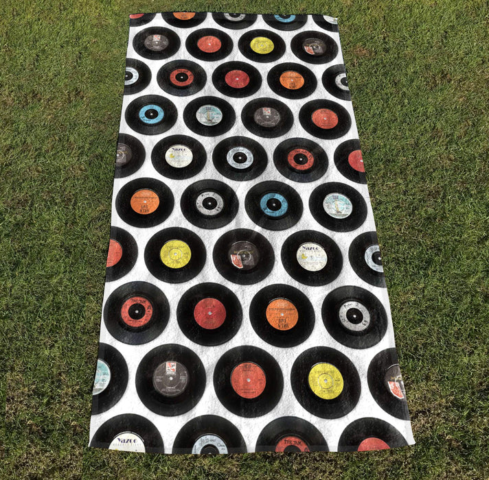 a towel with image of 7 inch vinyl records in a mosaic pattern, the towel laid out on grass