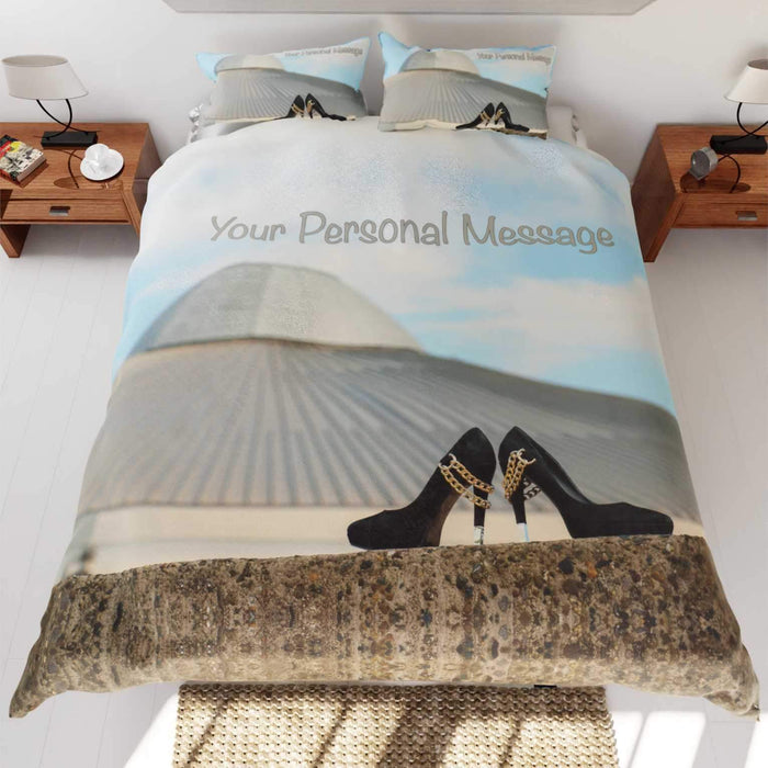 A duvet cover on a bed, the duvet cover having an image of a building skyline with a pair of shoes in the foreground, the building has the shape of a UFO, along with printed personal message
