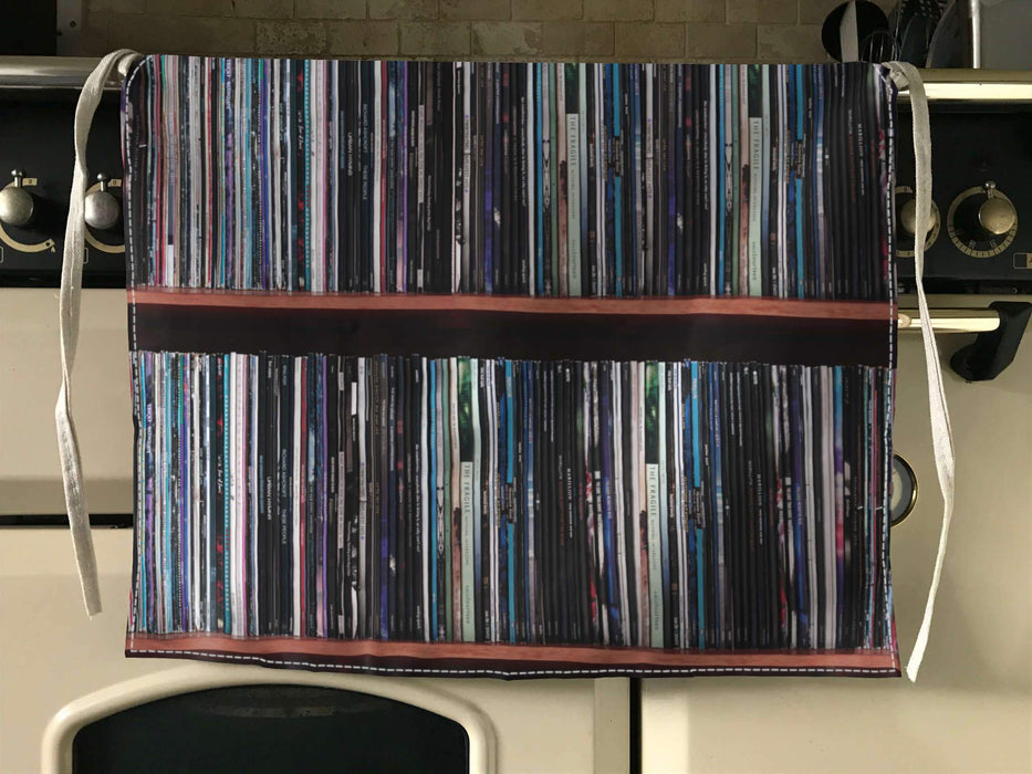 an apron folded over a kitchen cooker, the apron having images of lots of vinyl records in a record case