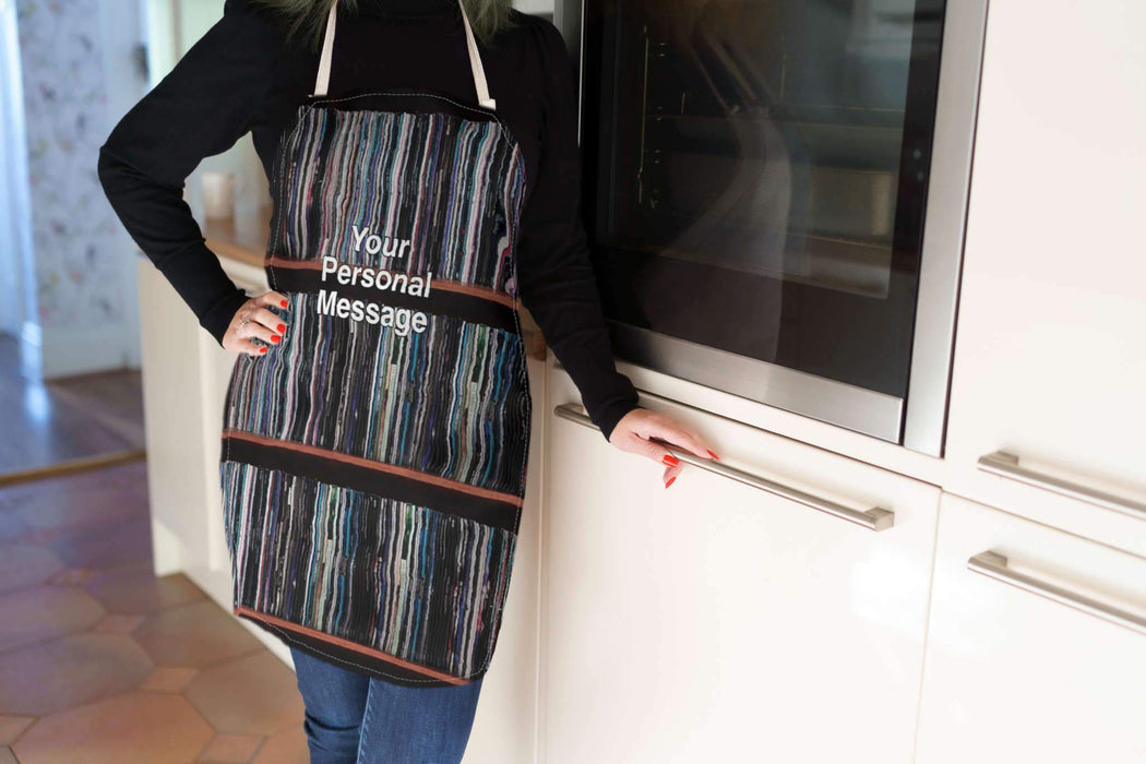 a women wearing an apron, stood in a kitchen, the apron having images of lots of vinyl records in a record case, with a personalised message printed